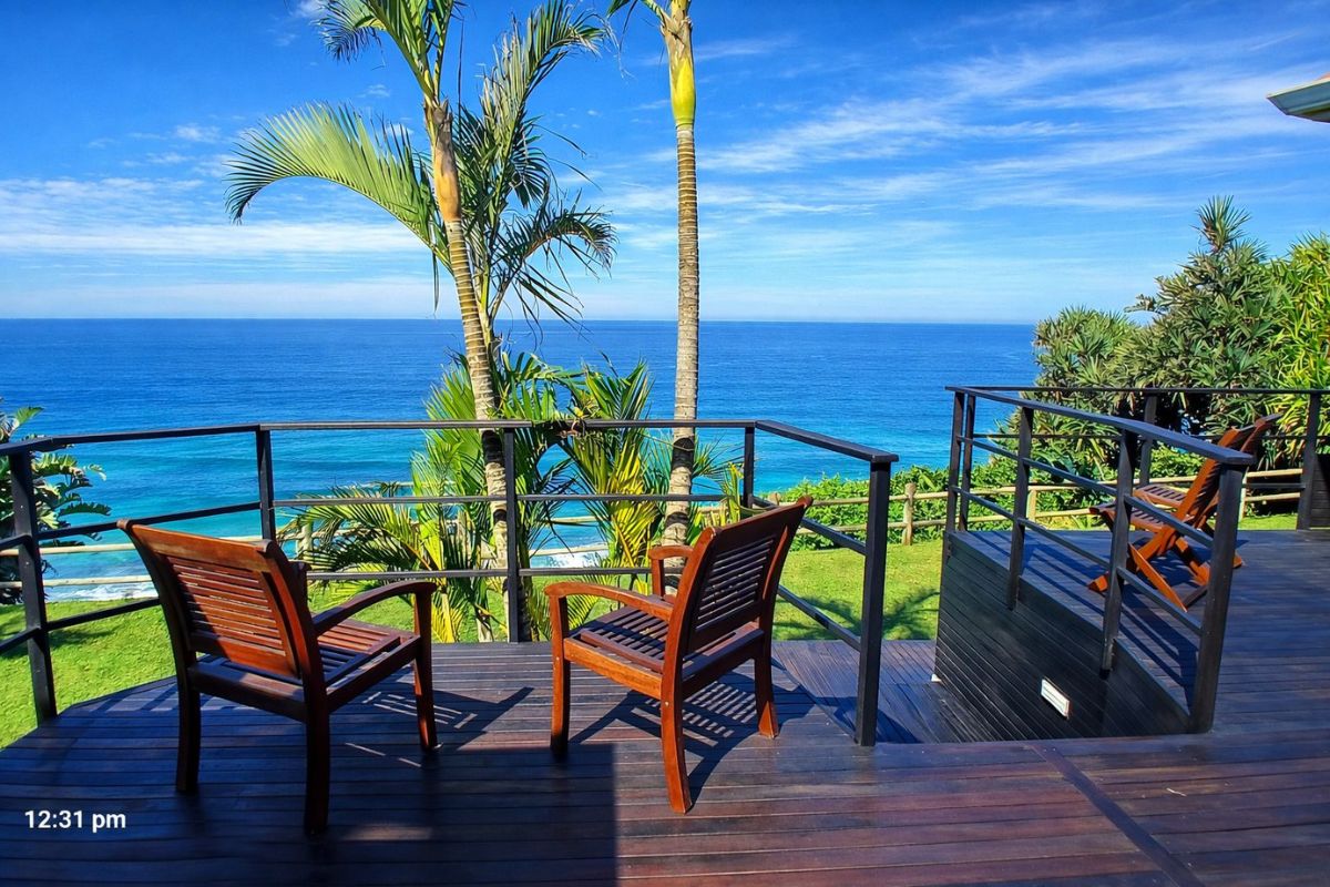 Relax on a wooden deck overlooking the blue ocean, framed by palm trees and sea-facing views from The Tides Inn B&B on the Bluff.