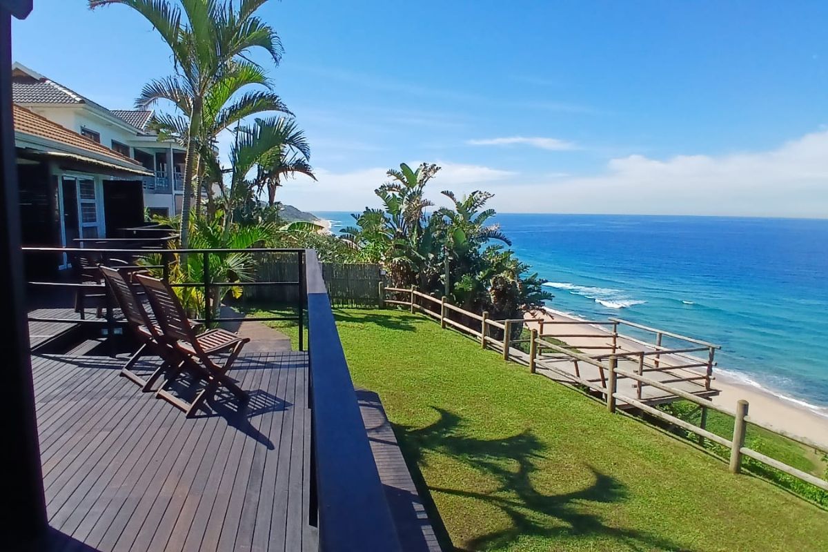 Sunlit ocean panorama at The Tides Inn on the Bluff, with palm trees, green lawn and a deck overlooking Durban’s Indian Ocean coastline.